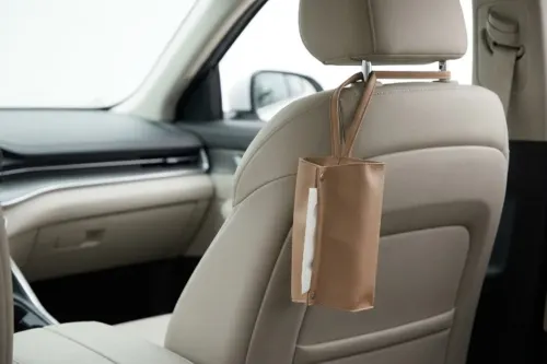 A minimalist PU leather tissue pouch with a strap, hanging conveniently from a car seat headrest in a clean interior.